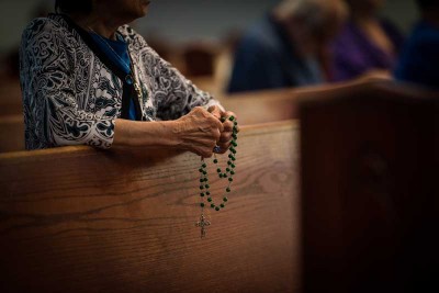 woman praying the rosary in church